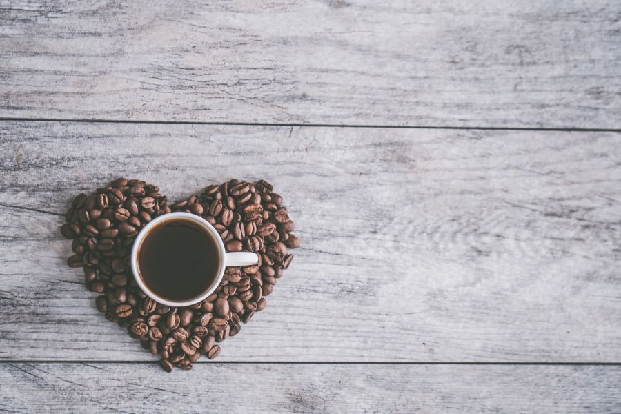 coffee filled white ceramic mug beside brown coffee beans on beige wooden surface