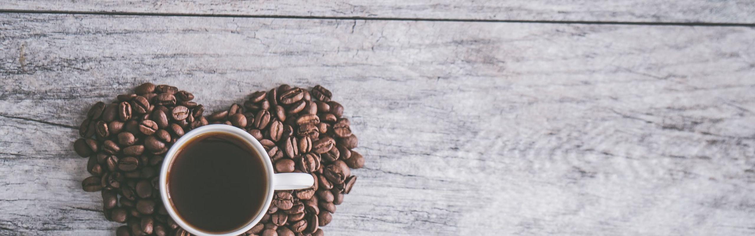 coffee filled white ceramic mug beside brown coffee beans on beige wooden surface